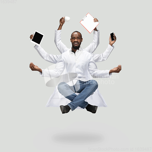 Image of Handsome multi-armed doctor levitating isolated on grey studio background with equipment