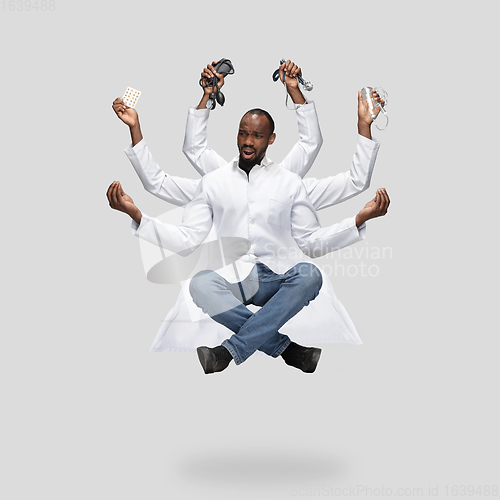 Image of Handsome multi-armed doctor levitating isolated on grey studio background with equipment