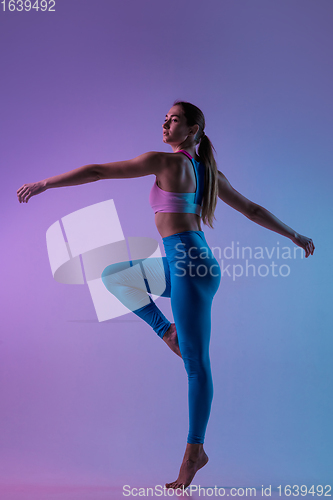 Image of Young sportive woman training isolated on gradient studio background in neon light. athletic and graceful