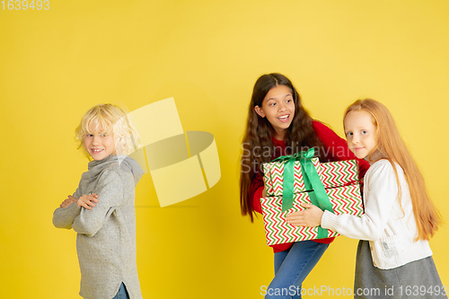 Image of Giving and getting presents on Christmas holidays. Group of happy smiling children having fun isolated on yellow studio background