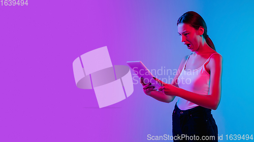 Image of Young caucasian woman\'s portrait on gradient blue-purple studio background in neon light