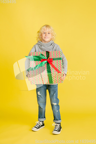 Image of Giving and getting presents on Christmas holidays. Little boy having fun isolated on yellow studio background