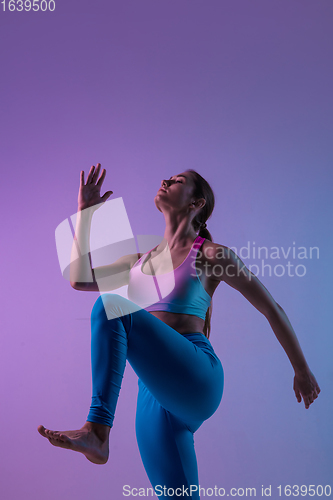 Image of Young sportive woman training isolated on gradient studio background in neon light. athletic and graceful