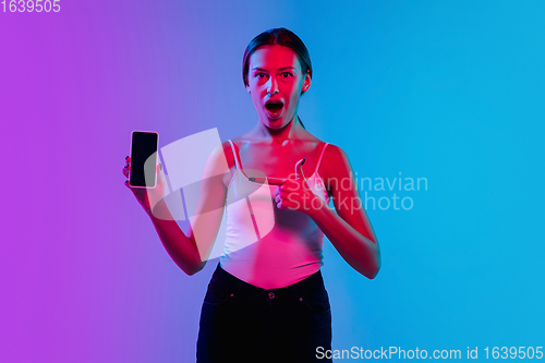 Image of Young caucasian woman\'s portrait on gradient blue-purple studio background in neon light