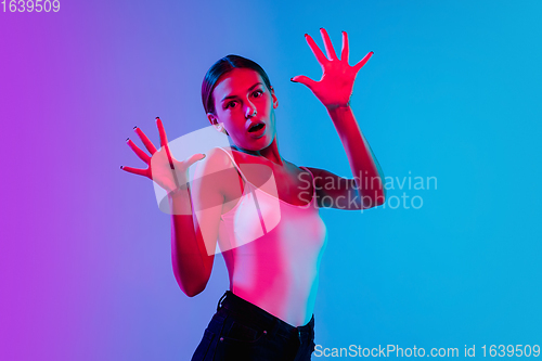 Image of Young caucasian woman\'s portrait on gradient blue-purple studio background in neon light