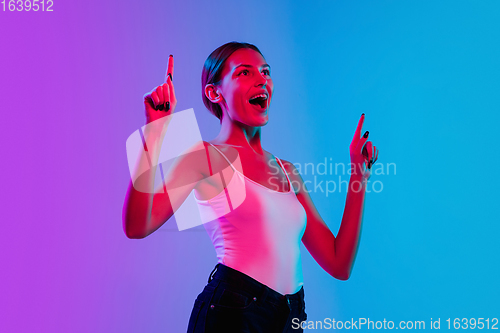 Image of Young caucasian woman\'s portrait on gradient blue-purple studio background in neon light