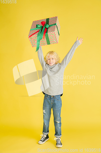 Image of Giving and getting presents on Christmas holidays. Little boy having fun isolated on yellow studio background
