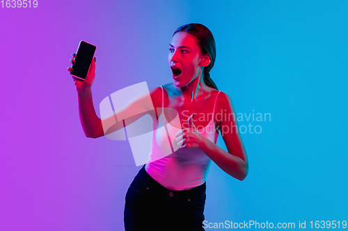 Image of Young caucasian woman\'s portrait on gradient blue-purple studio background in neon light