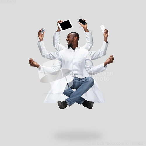 Image of Handsome multi-armed doctor levitating isolated on grey studio background with equipment