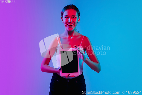 Image of Young caucasian woman\'s portrait on gradient blue-purple studio background in neon light