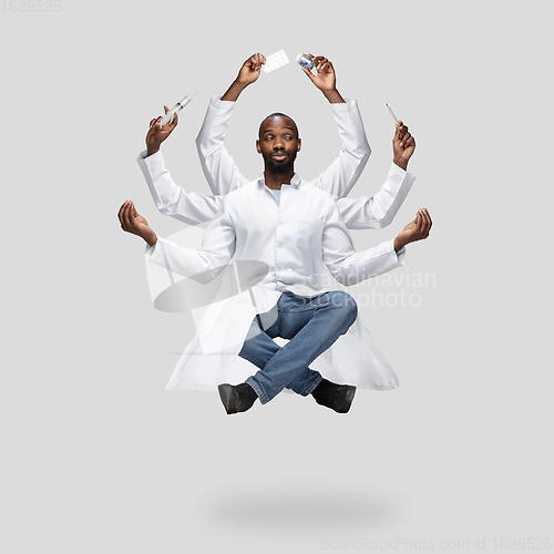 Image of Handsome multi-armed doctor levitating isolated on grey studio background with equipment