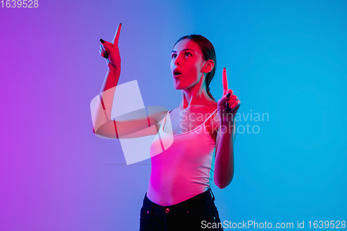 Image of Young caucasian woman\'s portrait on gradient blue-purple studio background in neon light