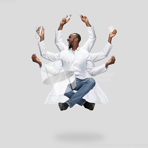 Image of Handsome multi-armed doctor levitating isolated on grey studio background with equipment