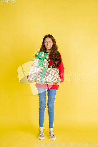 Image of Giving and getting presents on Christmas holidays. Teen girl having fun isolated on yellow studio background