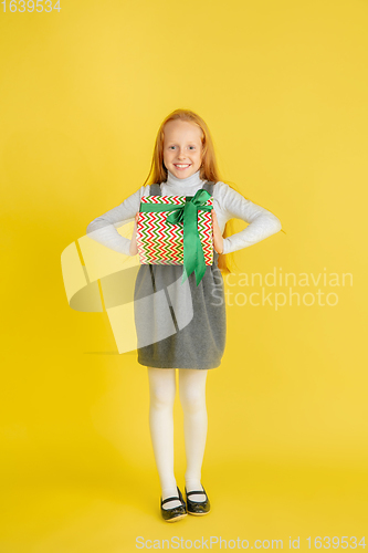 Image of Giving and getting presents on Christmas holidays. Teen girl having fun isolated on yellow studio background