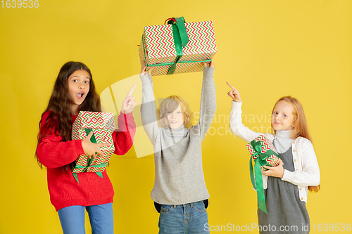 Image of Giving and getting presents on Christmas holidays. Group of happy smiling children having fun isolated on yellow studio background