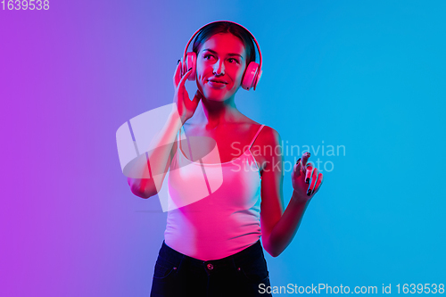 Image of Young caucasian woman\'s portrait on gradient blue-purple studio background in neon light