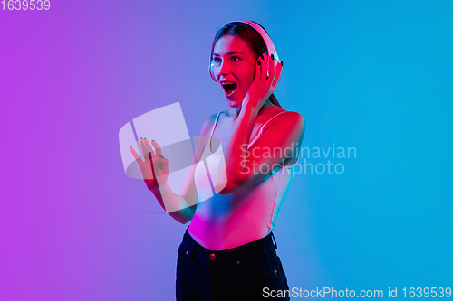 Image of Young caucasian woman\'s portrait on gradient blue-purple studio background in neon light
