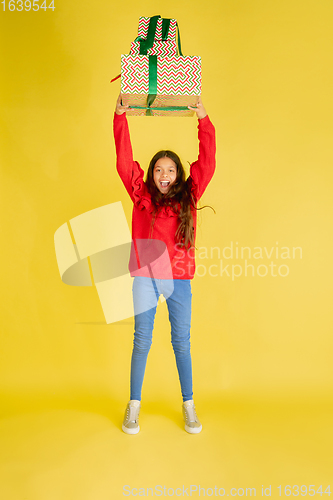 Image of Giving and getting presents on Christmas holidays. Teen girl having fun isolated on yellow studio background