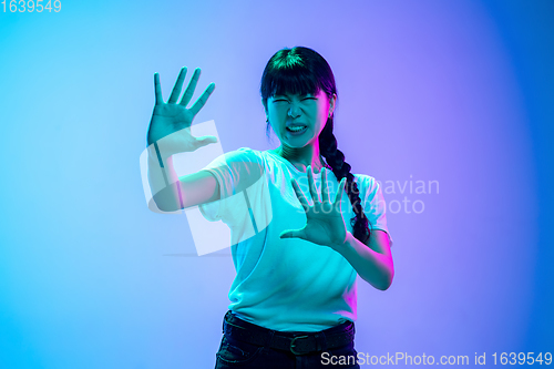 Image of Young asian woman\'s portrait on gradient blue-purple studio background in neon light