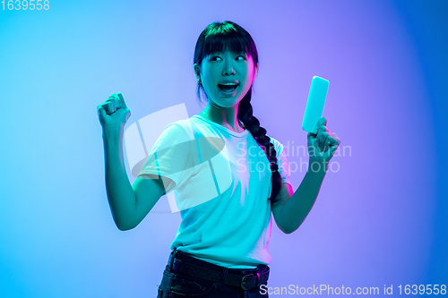 Image of Young asian woman\'s portrait on gradient blue-purple studio background in neon light