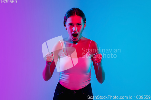 Image of Young caucasian woman\'s portrait on gradient blue-purple studio background in neon light