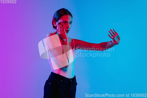 Image of Young caucasian woman\'s portrait on gradient blue-purple studio background in neon light