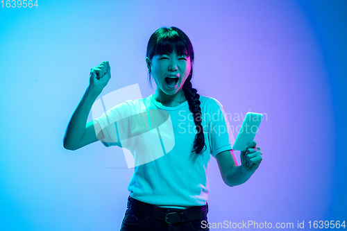 Image of Young asian woman\'s portrait on gradient blue-purple studio background in neon light