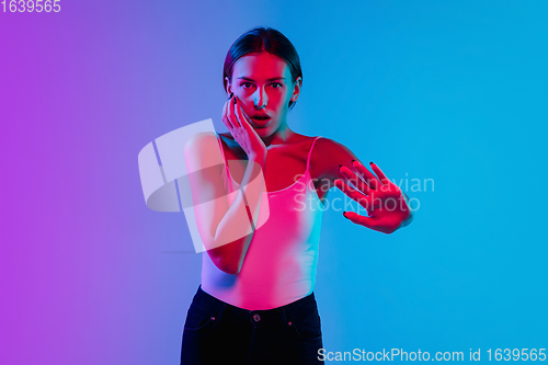 Image of Young caucasian woman\'s portrait on gradient blue-purple studio background in neon light