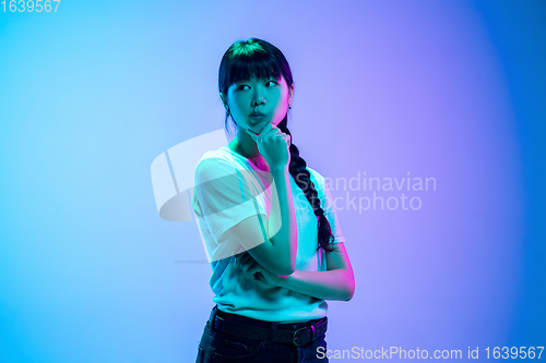 Image of Young asian woman\'s portrait on gradient blue-purple studio background in neon light