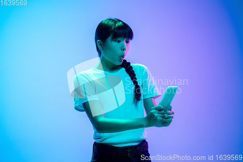 Image of Young asian woman\'s portrait on gradient blue-purple studio background in neon light