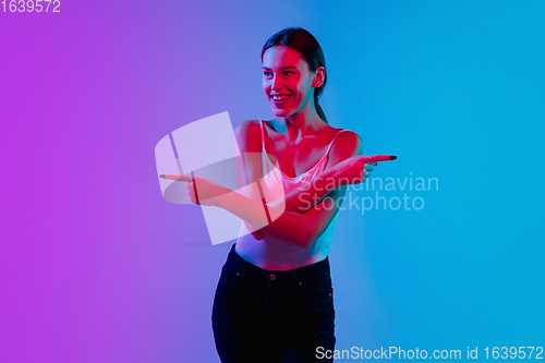 Image of Young caucasian woman\'s portrait on gradient blue-purple studio background in neon light