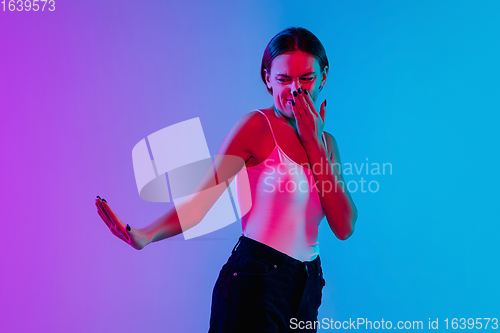 Image of Young caucasian woman\'s portrait on gradient blue-purple studio background in neon light