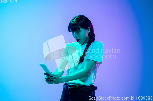 Image of Young asian woman\'s portrait on gradient blue-purple studio background in neon light