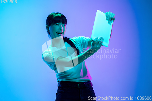 Image of Young asian woman\'s portrait on gradient blue-purple studio background in neon light