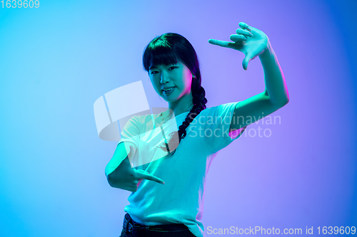 Image of Young asian woman\'s portrait on gradient blue-purple studio background in neon light