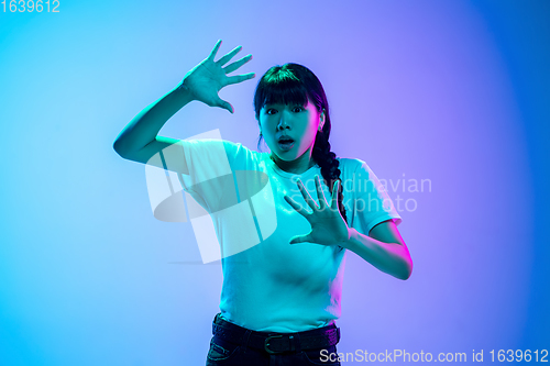 Image of Young asian woman\'s portrait on gradient blue-purple studio background in neon light