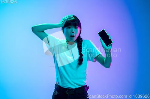 Image of Young asian woman\'s portrait on gradient blue-purple studio background in neon light
