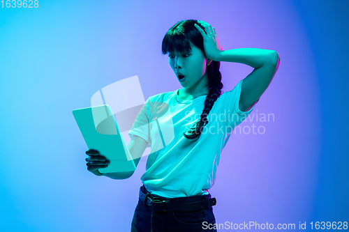 Image of Young asian woman\'s portrait on gradient blue-purple studio background in neon light