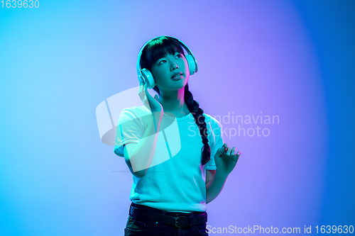 Image of Young asian woman\'s portrait on gradient blue-purple studio background in neon light