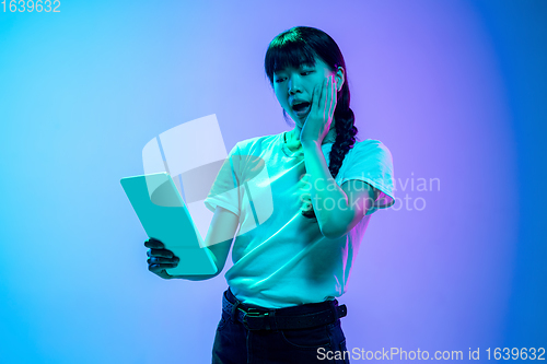 Image of Young asian woman\'s portrait on gradient blue-purple studio background in neon light