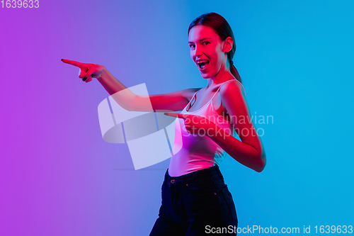 Image of Young caucasian woman\'s portrait on gradient blue-purple studio background in neon light