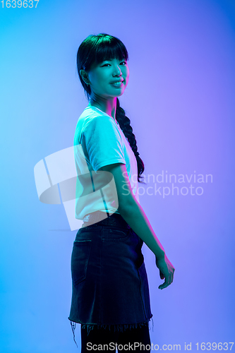 Image of Young asian woman\'s portrait on gradient blue-purple studio background in neon light