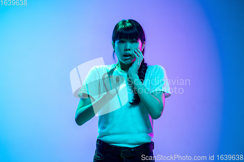 Image of Young asian woman\'s portrait on gradient blue-purple studio background in neon light