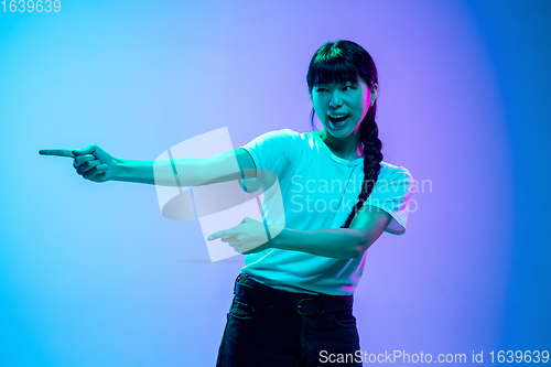 Image of Young asian woman\'s portrait on gradient blue-purple studio background in neon light