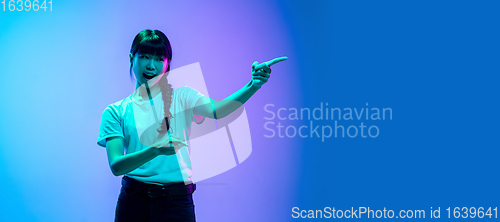 Image of Young asian woman\'s portrait on gradient blue-purple studio background in neon light