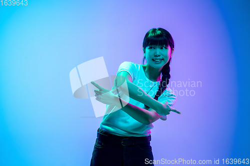 Image of Young asian woman\'s portrait on gradient blue-purple studio background in neon light