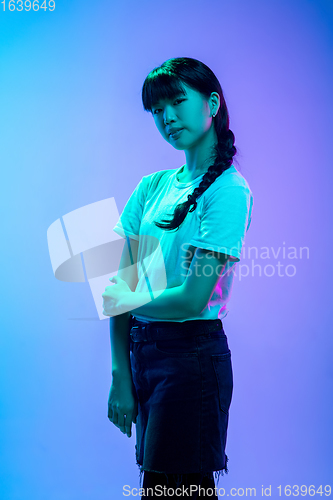 Image of Young asian woman\'s portrait on gradient blue-purple studio background in neon light