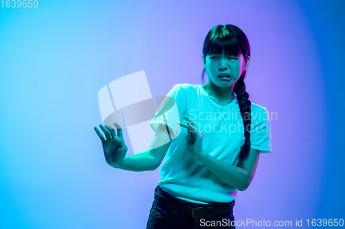 Image of Young asian woman\'s portrait on gradient blue-purple studio background in neon light