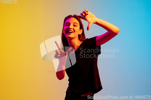 Image of Young caucasian woman\'s portrait on gradient blue-yellow studio background in neon light